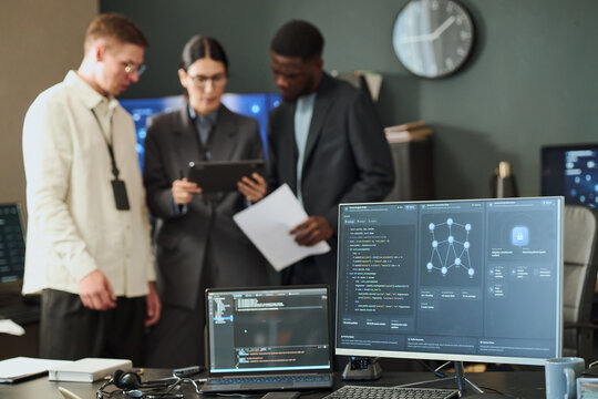 Multiethnic group of young adult IT professionals analyzing cyber security data on tablet in office. Concept suitable for cyber defense marketing and technology service advertising