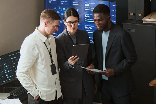 Multiethnic young adult colleagues analyzing data on tablet in cybersecurity office, collaborating on network safety. Perfect for IT security and corporate tech marketing