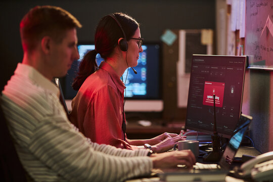 Caucasian young adult woman and man monitoring cyber threats on computer screens in cybersecurity office. Image suitable for data protection, network security and IT support advertising