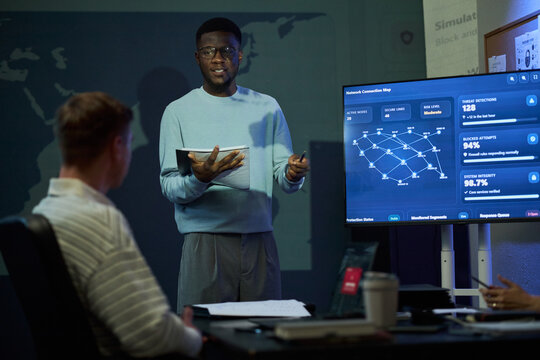 Young adult African American man explaining network security data on digital screen during corporate meeting. Visual useful for cybersecurity software marketing and IT defense training