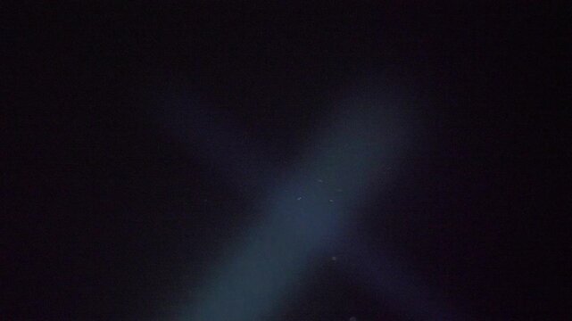 Focused flashlight lights deep sky above rooftops. Beam checks aerial space for unusual movement 