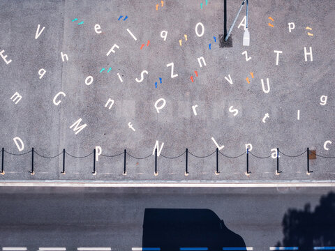Aerial view of the forecourt at the entrance to a primary school featuring scattered white letters and colorful footprints painted on the asphalt surface, Collegno, Piedmont, Italy.