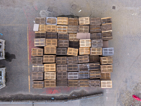 Aerial view of a large stack of wooden shipping pallets arranged in a grid pattern on an asphalt surface in Lauriano, Piedmont, Italy.