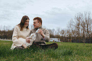 Fototapeta premium Couple outdoors with dog, affection and cozy atmosphere in a field setting, lifestyle moments of joy, grass underfoot, autumn light, candid smiles, serene countryside backdrop