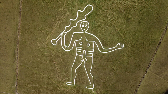 Aerial view of the Cerne Giant, a large hill figure carved into the chalk hillside, surrounded by green grass and rural fields in Cerne Abbas, England, United Kingdom.