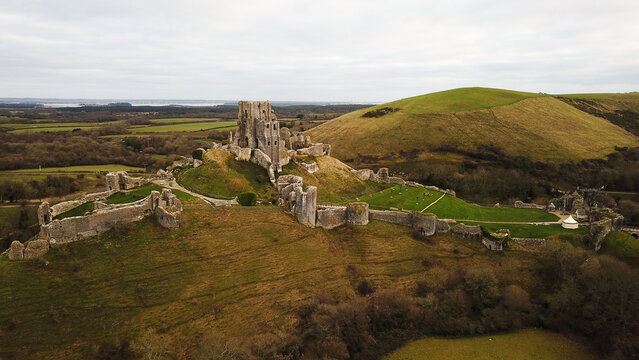 Aerial view of Corfe Castle ruins set on a grassy hill with stone walls and surrounding countryside in Corfe Castle, England, United Kingdom.