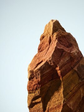 Dramatic red sandstone rock formation with striking natural erosion patterns under clear sky, desert landscape, geological wonder, warm sunlight lighting