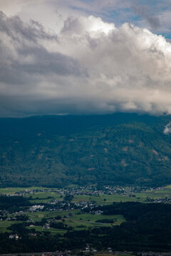 Aerial view of the valley landscape near Innsbruck, featuring green fields, scattered houses, and dense forests under a dramatic cloudy sky in the Alps, Innsbruck, Tyrol, Austria.