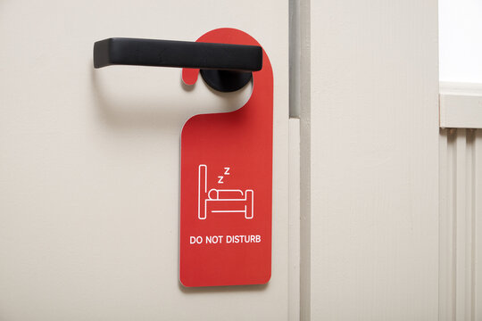 Closeup of red do not disturb sign hanging on black door handle in hotel