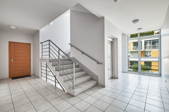 Modern staircase hall with elevator, wooden door, and panoramic window.