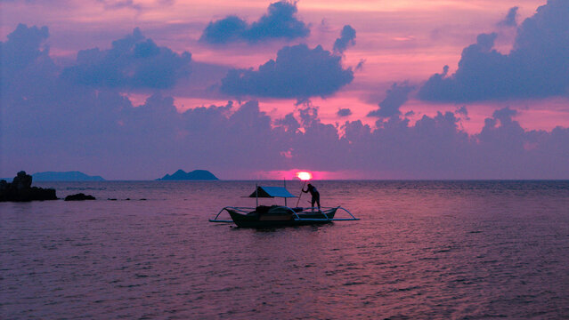 Aerial view of a traditional outrigger boat with a fisherman on the calm sea during a vibrant purple sunset in Busuanga, Mimaropa, Philippines.