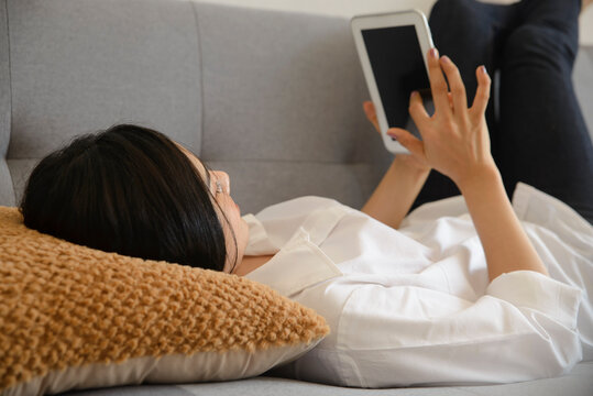 Woman using and holding tablet with finger, touching the screen during leisure time in comfortable living room.  Female relaxing on sofa at home, Lifestyle and technology concept.