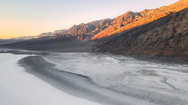 Aerial view of Badwater Basin salt flats surrounded by rugged mountains under warm golden hour light in Inyo County, California, United States.