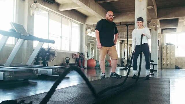 Two people train with battle ropes in a spacious gym, surrounded by treadmills and gear, focusing on strength and cardio