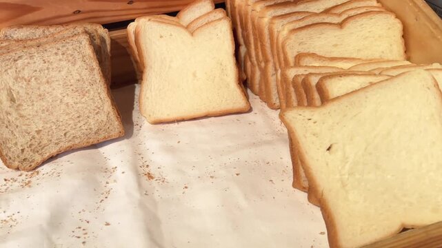 Video of sliced wheat and white toast bread stacked upright in a wooden bakery display bin