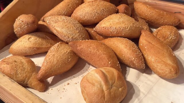 Video of freshly baked golden brown oval bread rolls displayed in a rustic wooden bakery tray