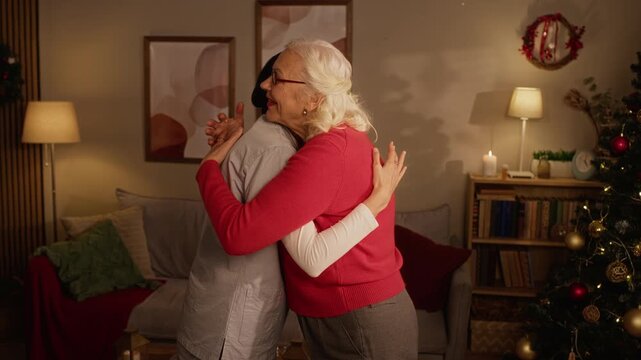 Senior Caucasian woman embracing adult female nurse near Christmas tree at home. Clip ideal for home healthcare campaigns, eldercare service promotions, and holiday companion support commercials