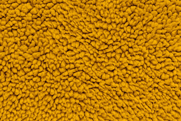 A full-frame, detailed close-up shot of soft mustard yellow sherpa fleece fabric, showing a fuzzy, curly teddy bear texture from a top-down view. Concept of warmth, comfort, cozy textile © DariaR