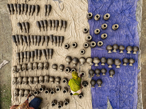 Aerial view of a person in a green sari arranging rows of clay pots drying on beige and blue mats in Kushtia, Khulna Division, Bangladesh.