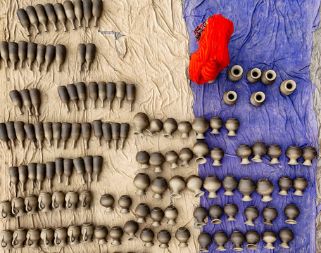 Aerial view of handmade clay pottery arranged in rows on fabric mats to dry in the sun, with a person in red clothing working among the items in Kushtia, Khulna Division, Bangladesh.
