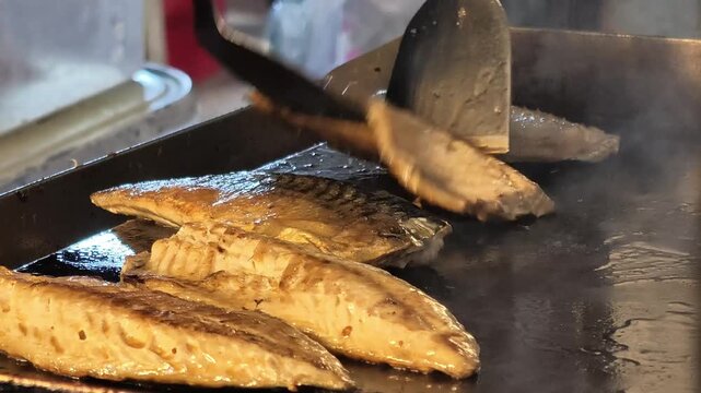 Chef Flipping Grilled Mackerel Fillets on Flat Top Grill