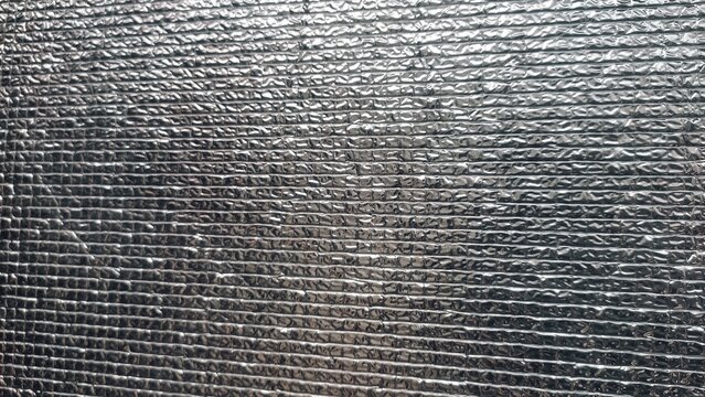 A high-detail close-up shot of a metallic silver thermal insulation sheet featuring a embossed textured grid pattern