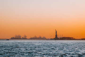 Statue of Liberty silhouette across New York Harbor at orange sunset © Ivan