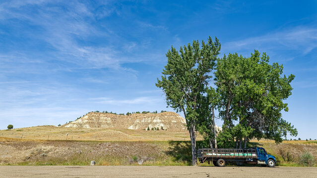 Panorama of a flatbed truck with a load of pipes parked under a tree at a rest stop by a butte in Montana, USA