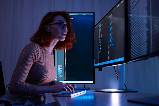 Female programmer reviews computer code on multiple screens during a focused coding session, illustrating software engineering, development, testing, and digital technology work.