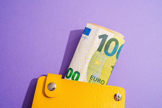Yellow wallet with rolled euro notes on purple studio background