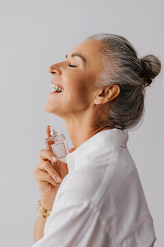 Mature woman applying perfume, smiling with joy and natural elegance