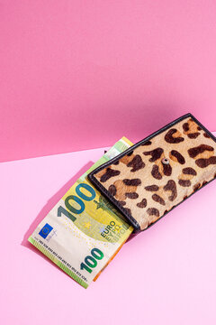 Leopard print wallet holding 100 euro banknote on pink studio