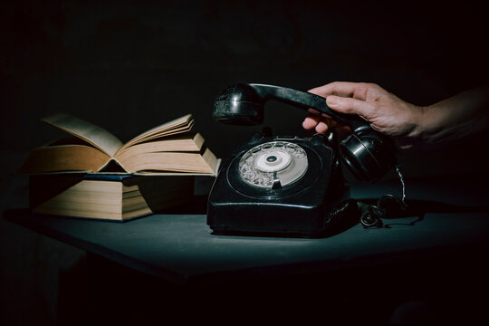 Person Lifting a Rotary Phone Near an Open Book
