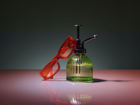 Retro orange sunglasses resting on a vintage green glass spray