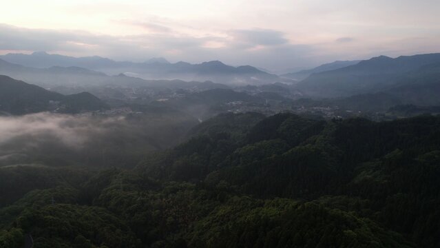Aerial view of Takachiho no asa with rolling hills covered in lush green forests and morning mist under a soft sky in Takachiho, Miyazaki, Japan.