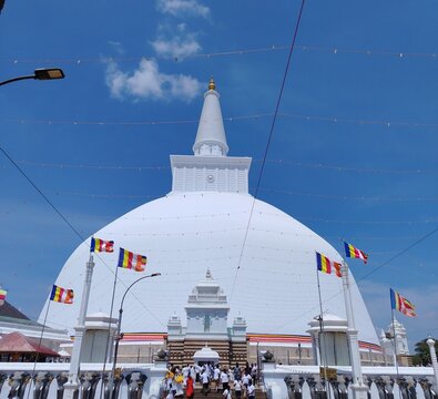 Ruwanwelisaya Stupa In Anuradhapura Sri Lanka, Sacred Buddhist Temple With Devotees And Buddhist Flags Under Blue Sky