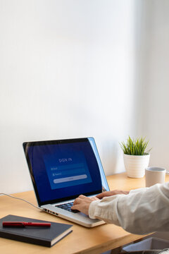 Vertical shot of person typing on laptop screen showing sign in login interface on desk