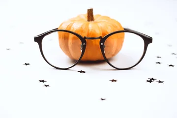 Orange pumpkin behind black eyeglasses with star confetti on white. Funny Halloween idea for optician, eyewear sale or school. © Anna Efetova