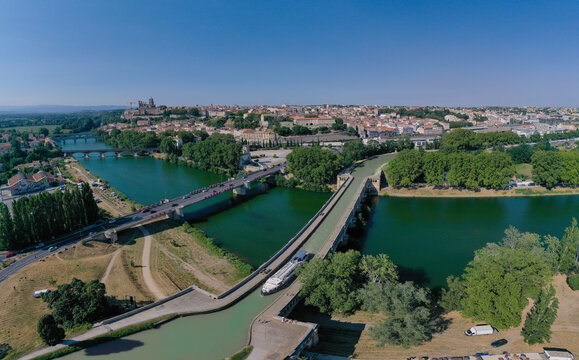 Aerial view of the Orb Aqueduct carrying the Canal du Midi over the River Orb, with the historic city of Beziers in the background. Beziers, Occitanie, France.