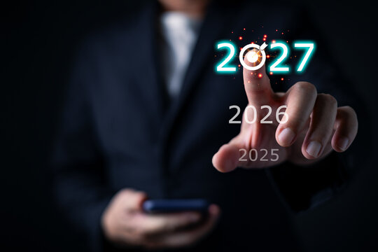 Businessman pointing at glowing year 2027 target dartboard over 2026 and 2025, representing strategic future planning, business goal forecasting, and corporate achievement.