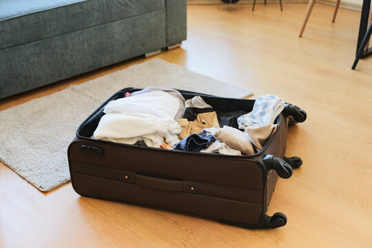 An open luggage packed with clothes lying on a wooden floor in a living room before a trip.