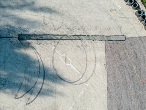 Aerial view of a drift track featuring asphalt surface with black tire marks, white track markings, and shadows cast by nearby trees in Krimulda Parish, Sigulda Municipality, Latvia.