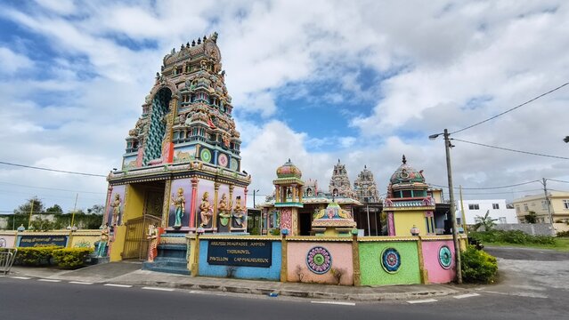 Colorful Hindu temple tower with intricate deity statues under a cloudy sky.