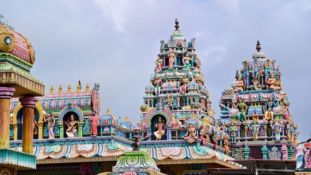 Colorful Hindu temple tower with intricate deity statues under a cloudy sky.