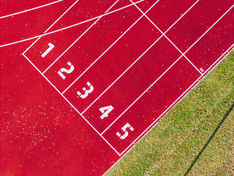Aerial view of the red running track at Krimulda Secondary School Stadium with numbered lanes and green grass borders in Ragana, Sigulda Municipality, Latvia.