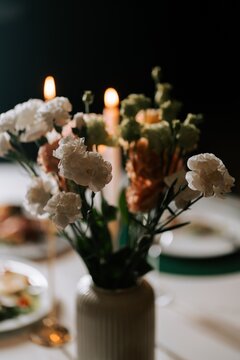 White carnations in a vase on a dining table with candles glowing during a dark evening dinner
