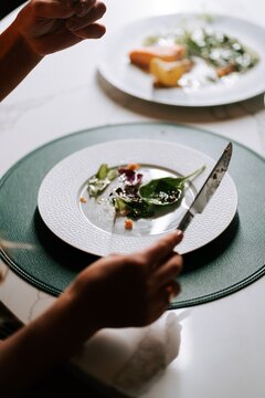 Person holding a knife and fork while preparing to eat a light salad meal during a lunch dining time