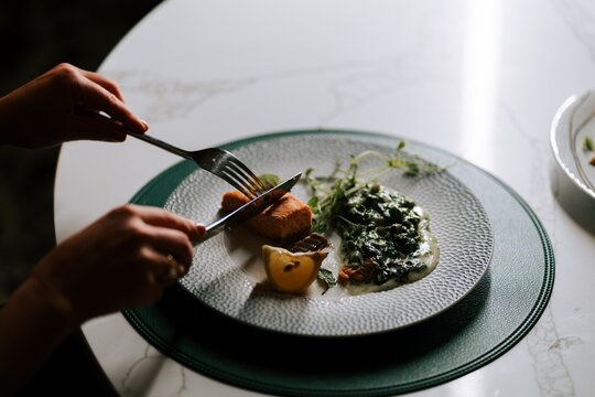 Person cutting a piece of grilled salmon with creamed spinach on a white plate during a fine dinner