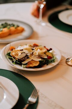 Fresh salad served with thin cheese slices on a white plate at a restaurant table during dinner time