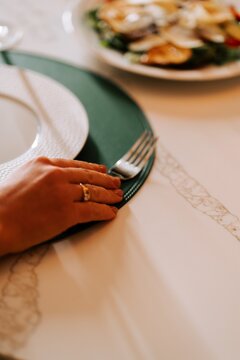 Person sitting at a dining table with a fork and a salad plate during a bright afternoon meal